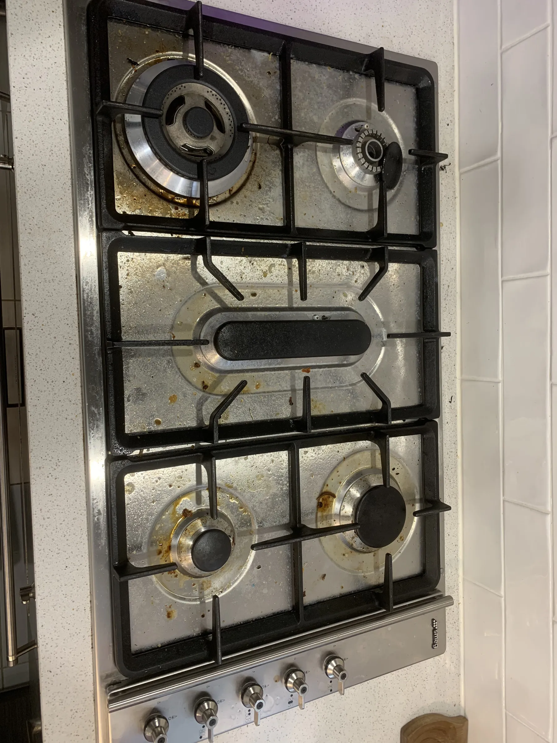 Stainless steel gas cooktop with burnt-on grease and food residue before cleaning
