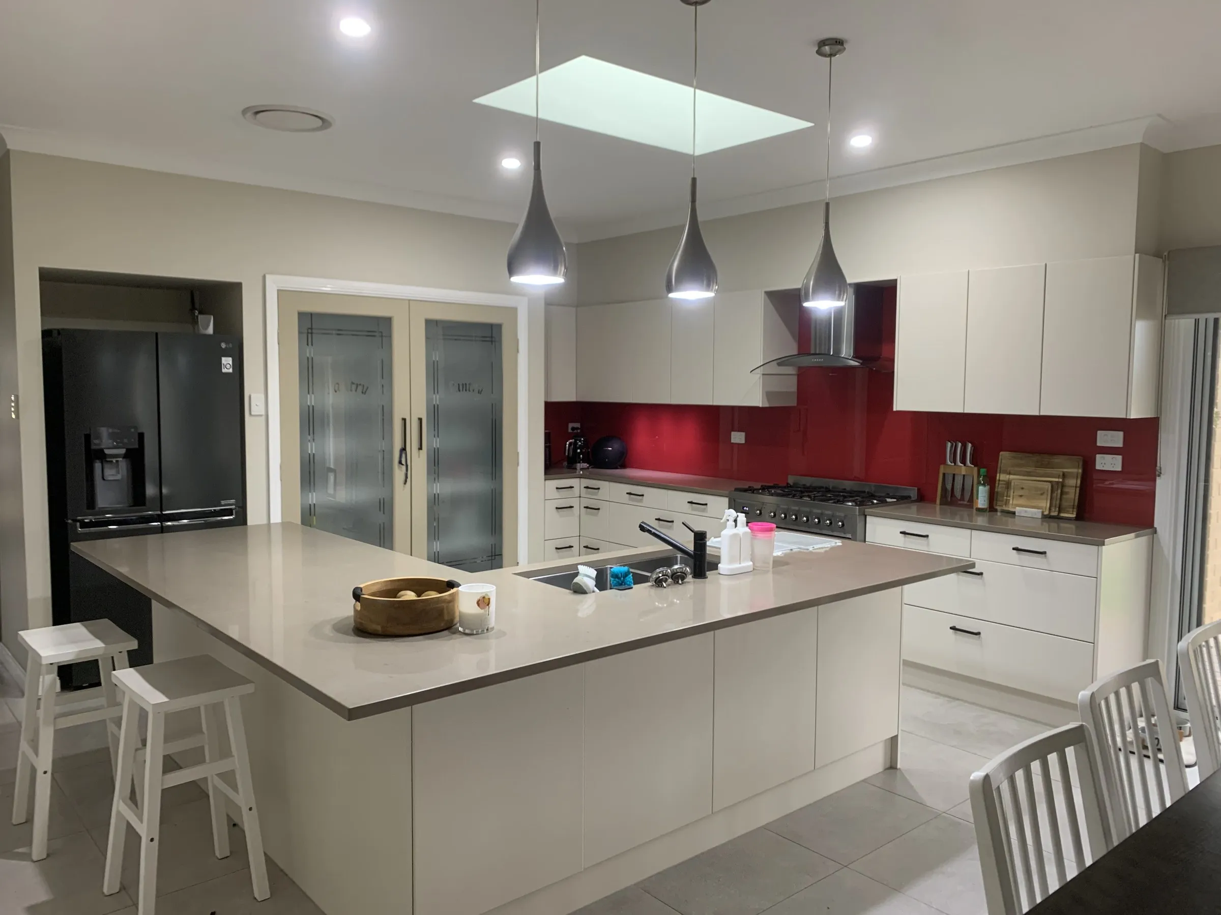 Open plan kitchen with a large island bench, pendant lights and a red glass splashback after cleaning