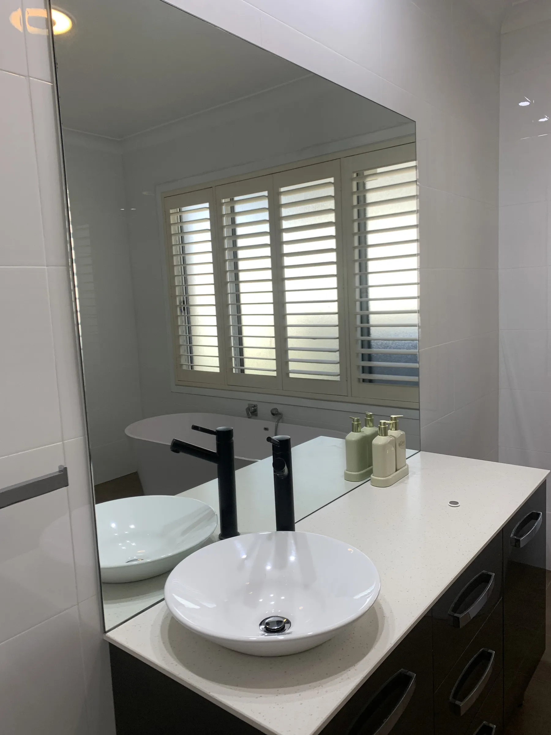 Bathroom vanity and mirror reflecting a freestanding bath and plantation shutters after cleaning