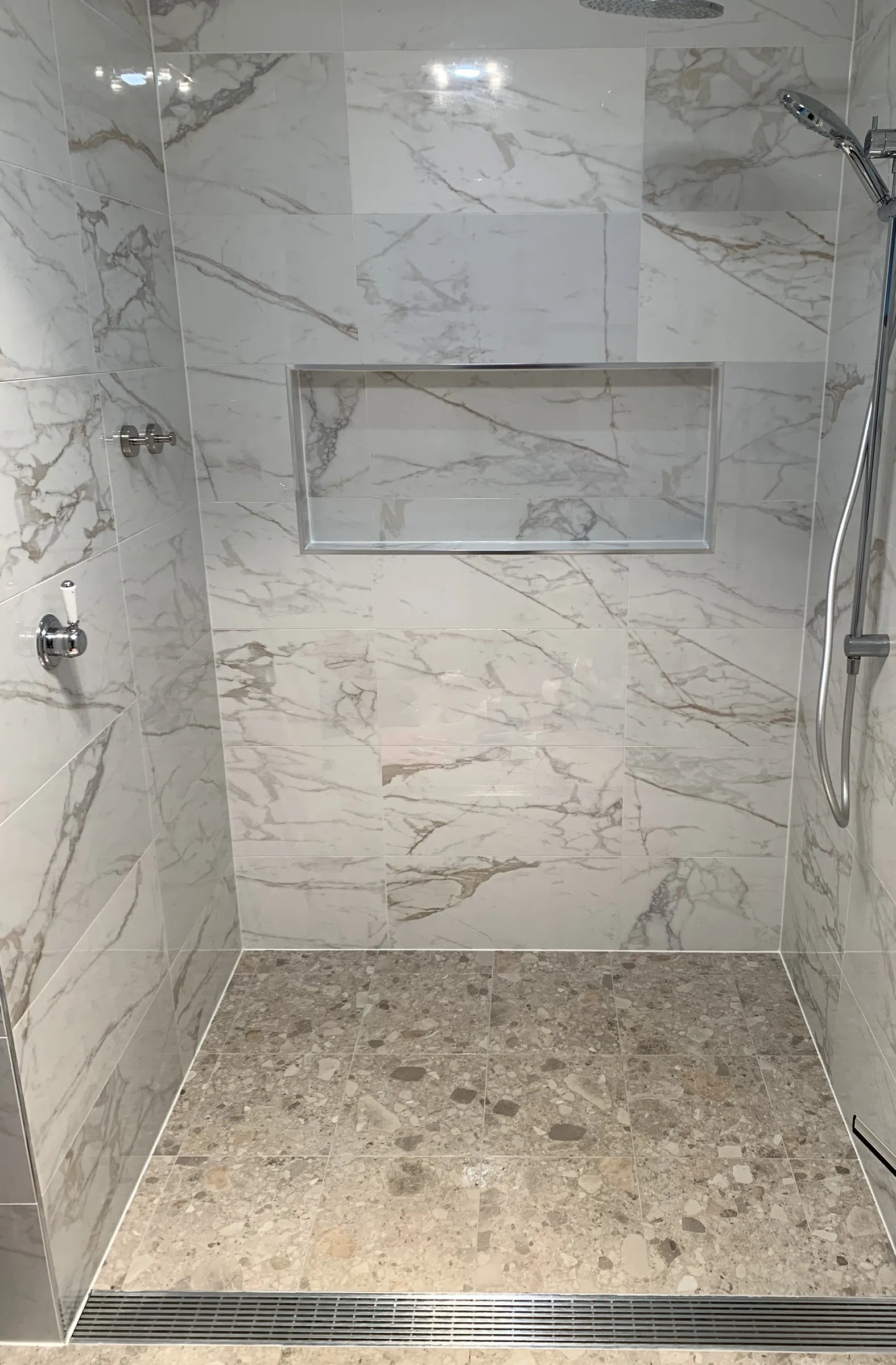 Walk in shower with marble look tiles, recessed niche and clean tiled floor