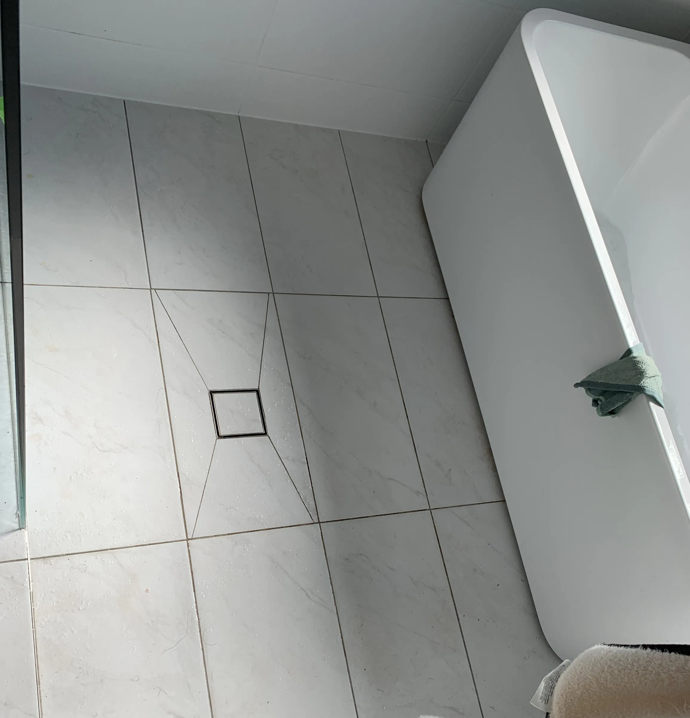 Bathroom floor beside a freestanding bath with hair and water marks before cleaning